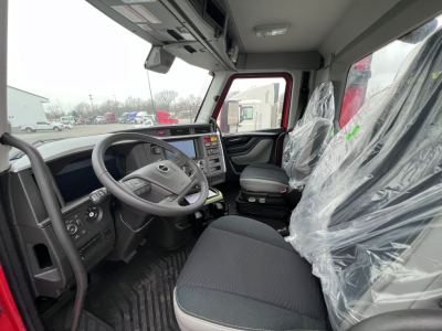 Truck cab interior of Volvo VNL showing steering wheel, dashboard, driver seat, and plastic-covered passenger seat. Visible controls and center console.