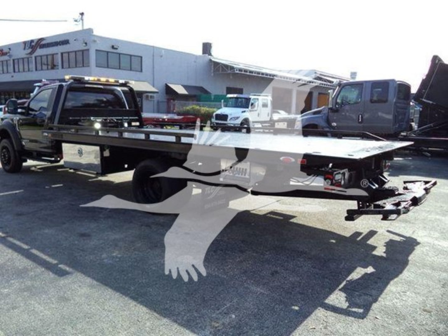Flatbed tow truck with extended bed on a Ford F-600 chassis, rollback configuration, side view showing dual rear wheels and towing equipment.