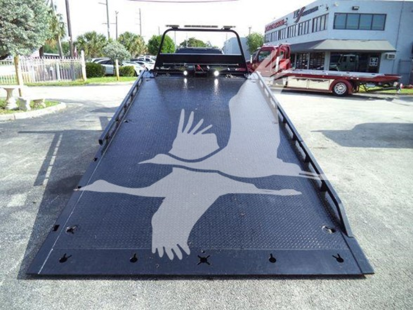 Truck bed of a 2022 Ford F600 rollback showing a metal flatbed with a painted white bird graphic and tie-down holes along the edges.