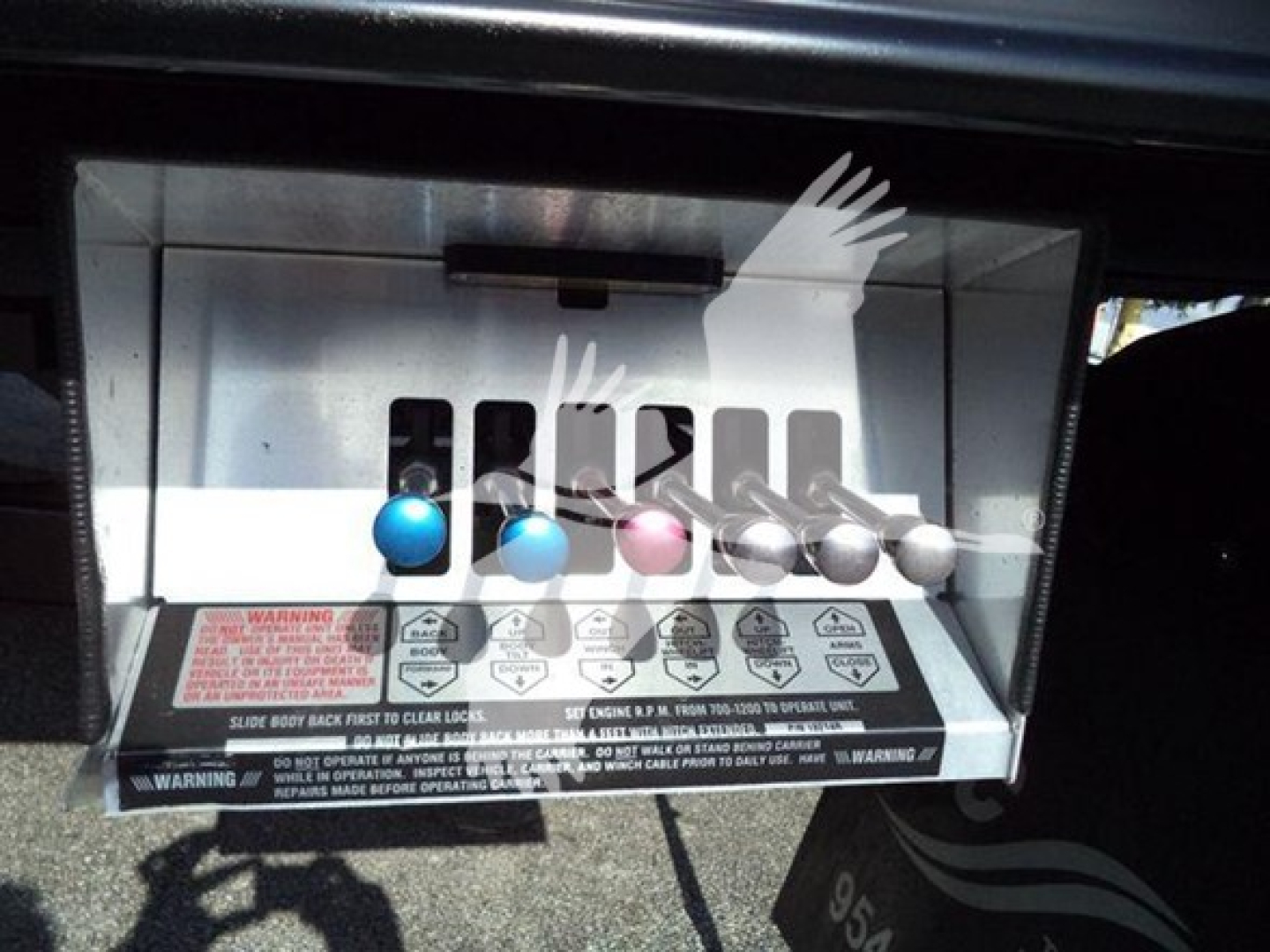 Control panel with multiple colored knobs and warning labels on a Ford F-600 rollback truck operator interface.