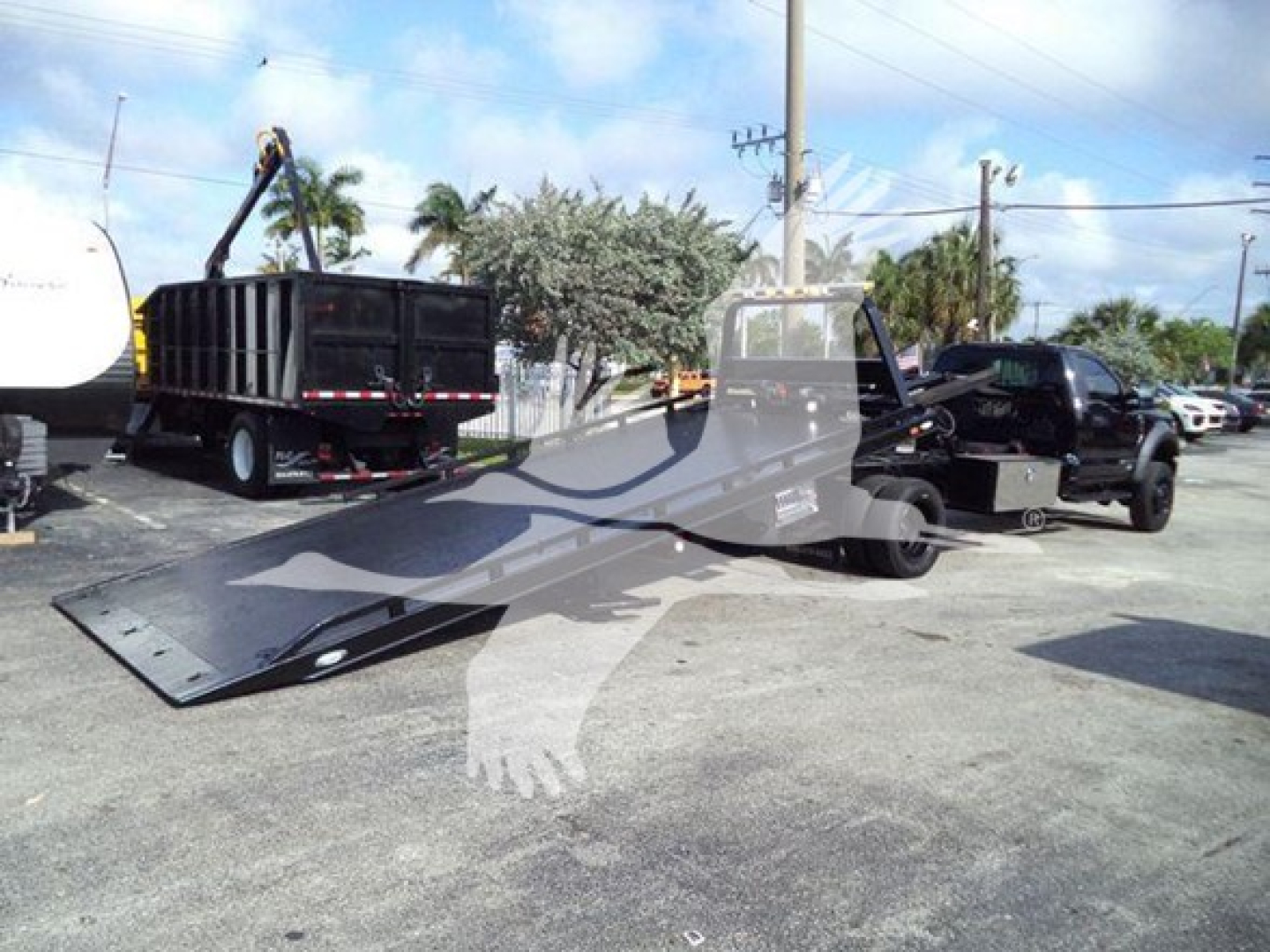 Ford F-600 rollback truck with extended flatbed and wheel-lift, black cab, and tow equipment in lot.