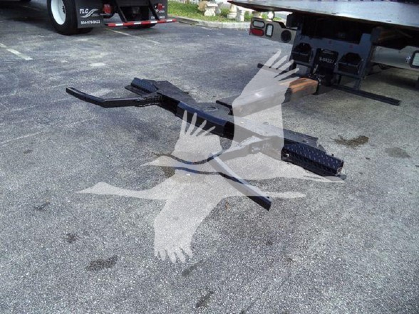 Ford F600 rollback truck with exposed hitch components on pavement; metal frame and steps visible near rear of tow rig.