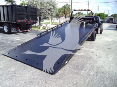 Truck tow rollback with long black steel ramp bed and Ford F-600 rear view showing flatbed with safety rails and dove watermark