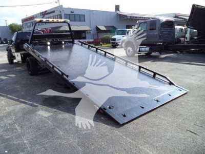 Truck bed rollback tilt deck showing metal surface and ramp on a Ford F-600 with other vehicles in lot.