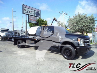 Ford F-600 rollback truck in dealership lot showing long flatbed and black accents with TLC logo watermark.