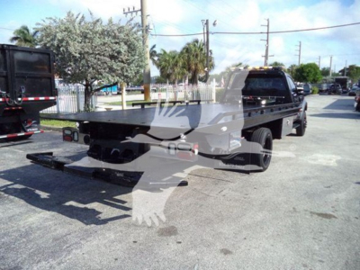 Flatbed rollback tow truck chassis with rear flat bed and black cab, visible tail lights and rear tires; no legible branding or text readable on the vehicle.