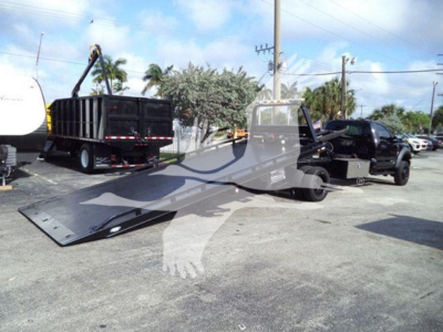 Ford F-600 rollback truck with extended flatbed and wheel-lift, black cab, and tow equipment in lot.