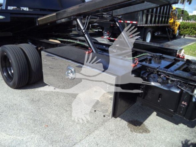 Ford F-600 rollback truck chassis showing toolbox and hydraulic components under the bed. Visible are the dual rear wheels, frame rails, toolbox with a recessed lock, hydraulic lines, and frame-mounted hardware.