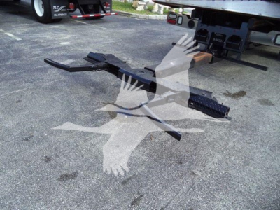 Ford F600 rollback truck with exposed hitch components on pavement; metal frame and steps visible near rear of tow rig.