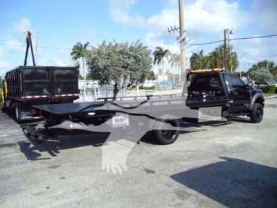Tow truck with flatbed and black tow truck, showing Ford F-600 chassis and rollback equipment. Visible text includes VIN area and stock number on plate; no legible brand labels besides Ford.