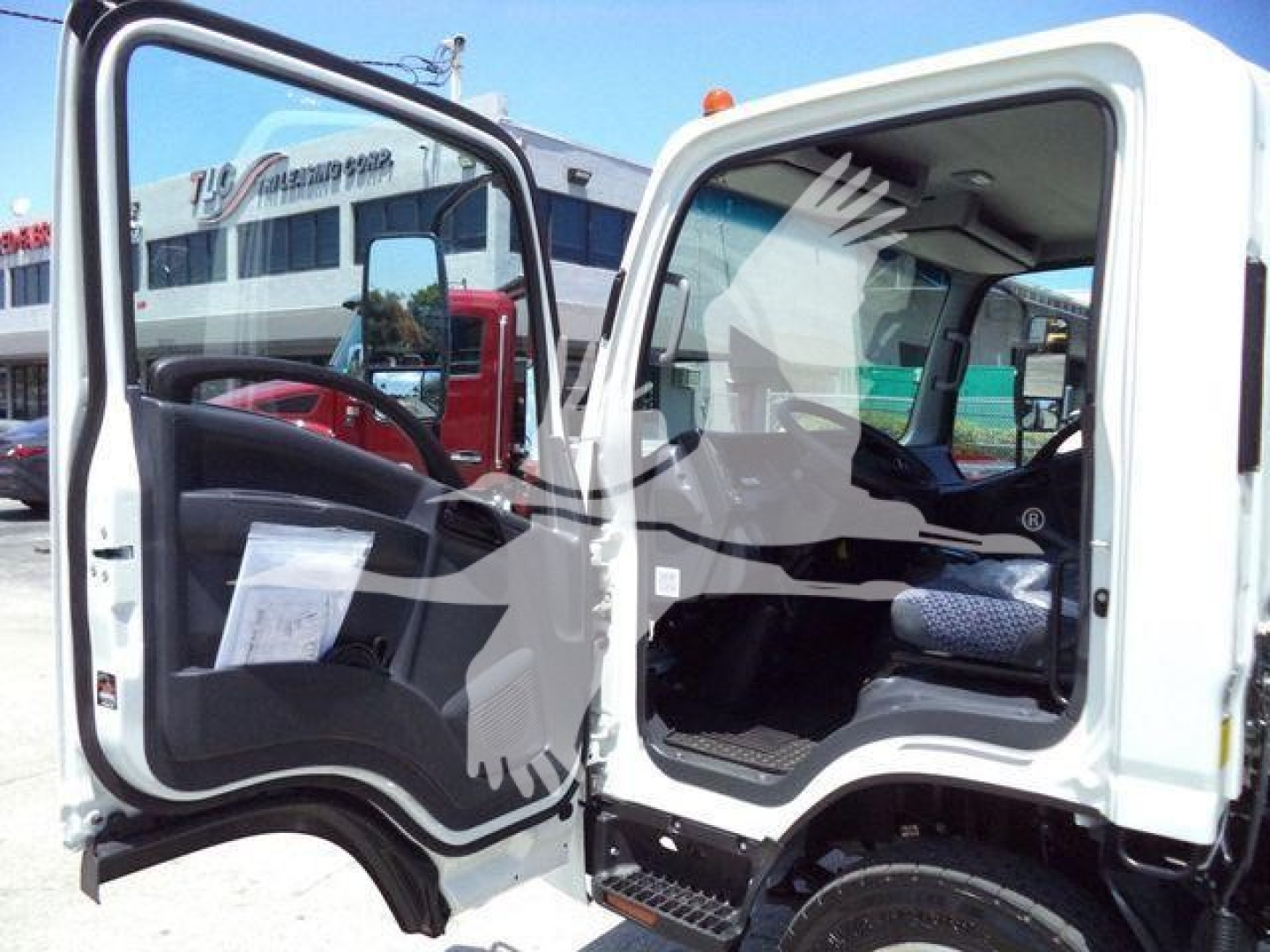 Isuzu NPR truck cab interior with open door showing steering wheel and seat; truck mirrors and other vehicles visible in background.