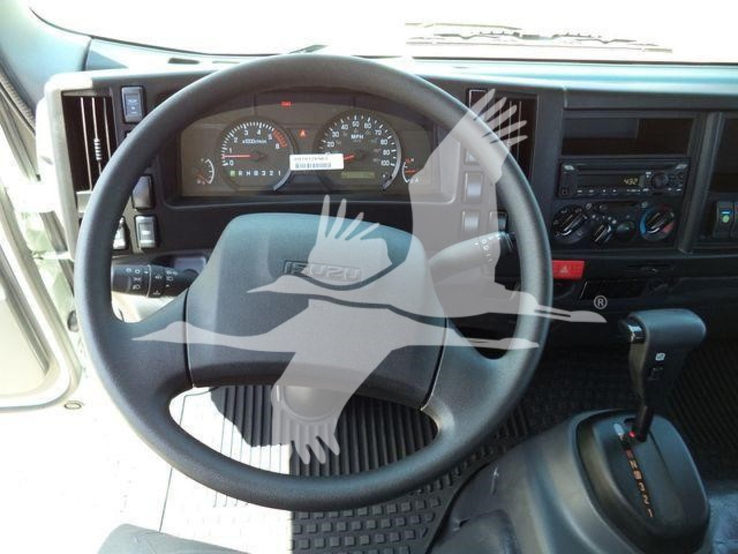 Isuzu NPRR cab interior showing steering wheel, dashboard gauges, and center console with gear shifter.