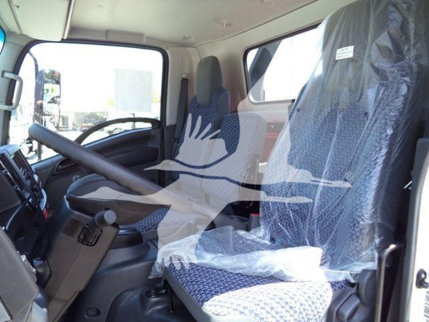 Isuzu NPRR truck cab interior view showing steering wheel, driver seat covered in protective plastic, and passenger seat with fabric pattern.
