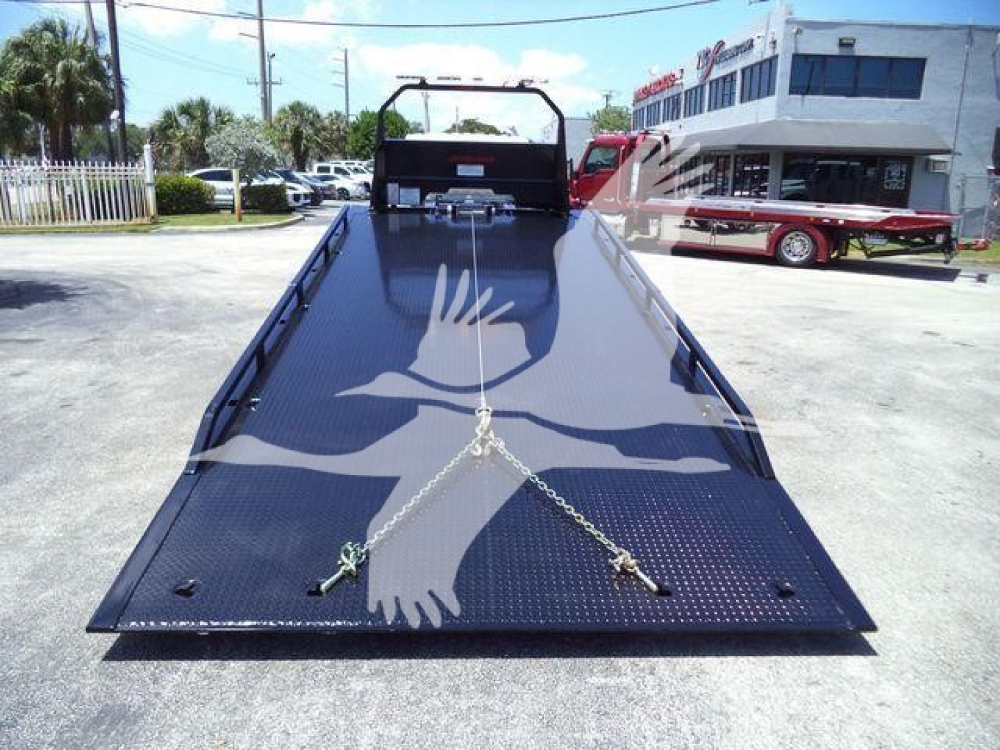 Isuzu NRRGAS22XLP rollback truck bed with a black diamond plate surface and tie-down chains, rear view.