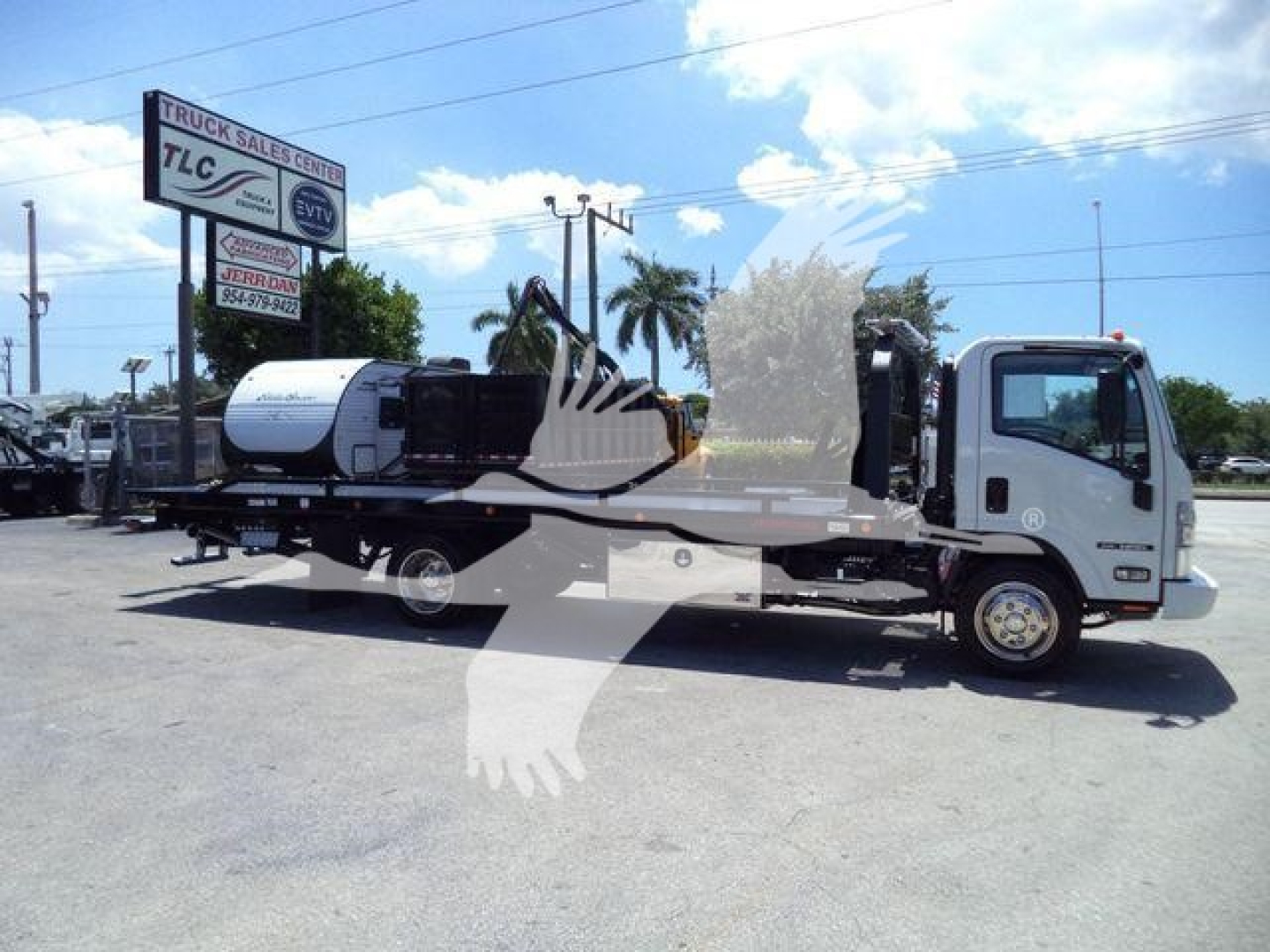 Isuzu NPR rollback tow truck with a flatbed and water tank, side view in a dealership lot.