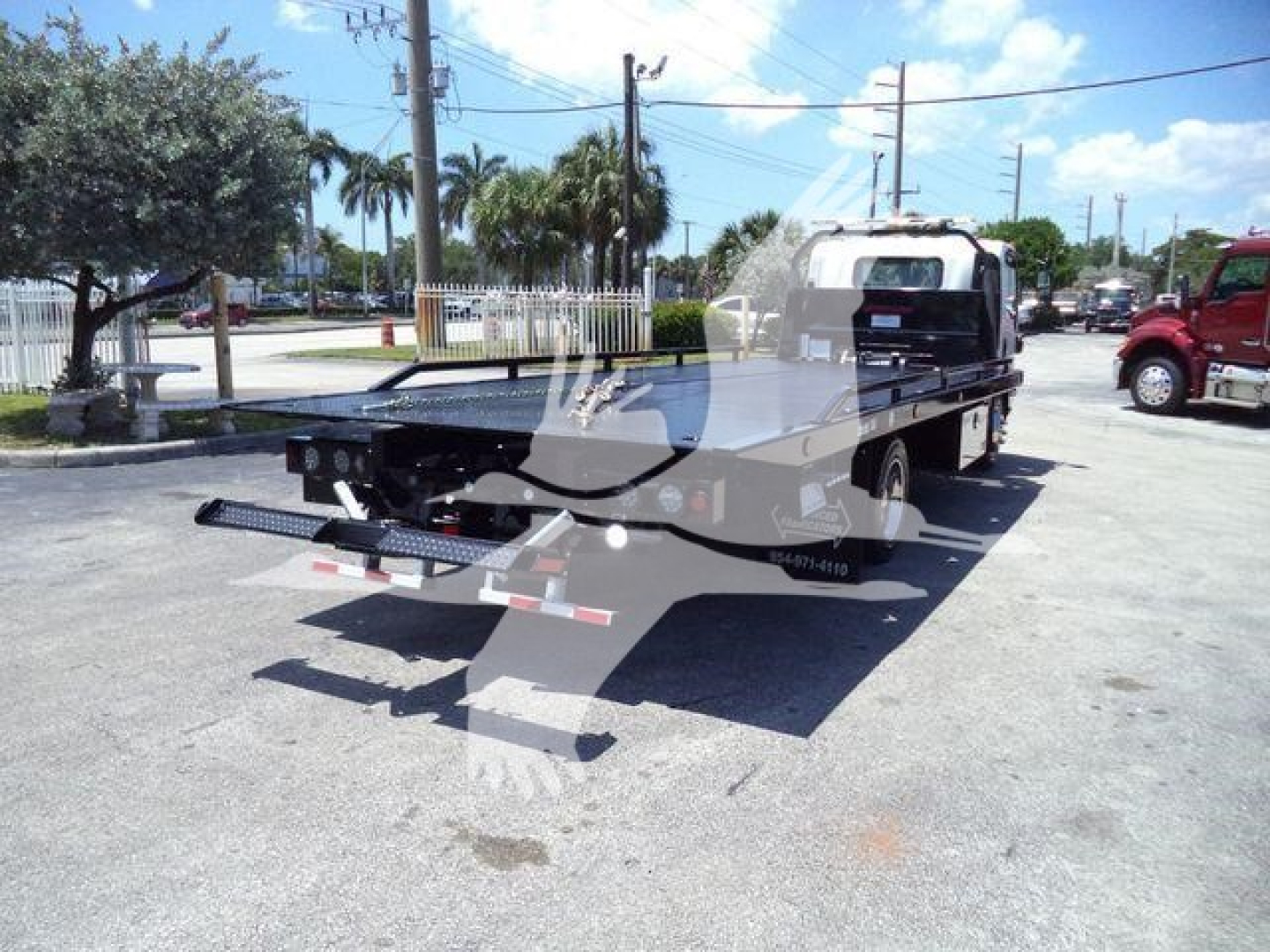 Isuzu NPRR rollback tow truck rear view showing flatbed and equipment, with decals and light bar.