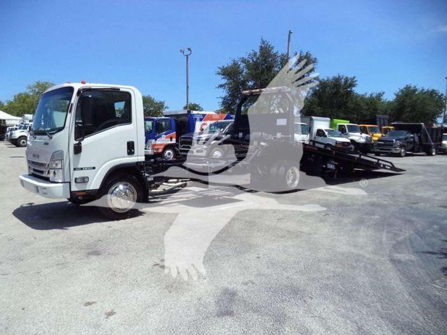 Isuzu NPR/RR rollback tow truck in a dealership lot with flatbed and loading equipment visible.