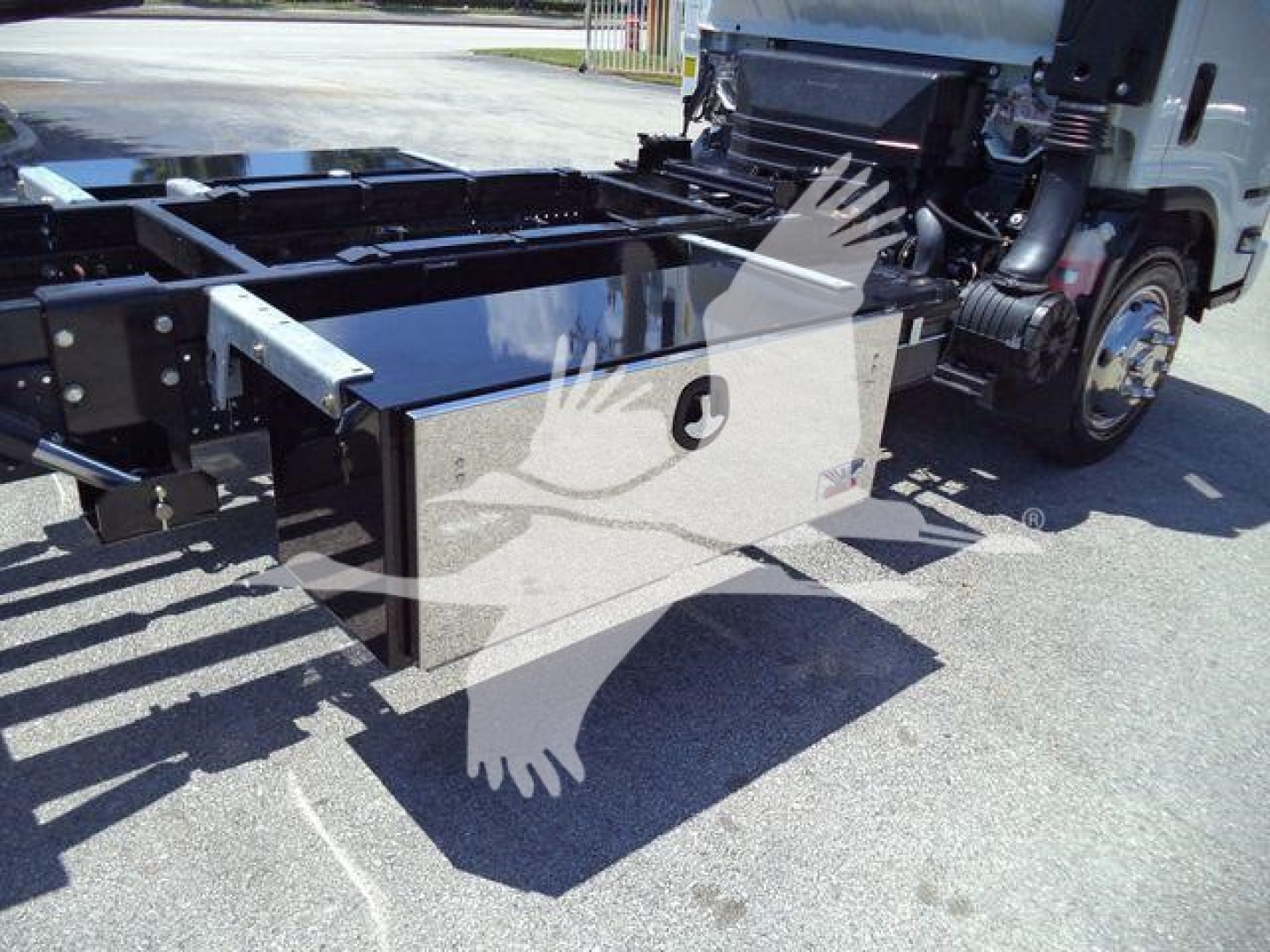 Isuzu NPRR rollback truck chassis side view showing metal frame, hydraulic components, and storage box under the cab.