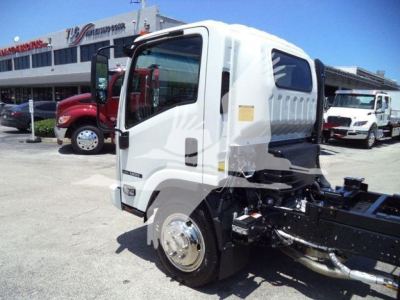 Isuzu NPR/NRR cab chassis in white beside dealership, with rollback equipment mounting and front wheel visible.