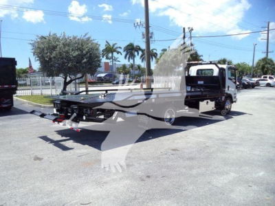Isuzu NPRR flatbed rollback tow truck in a dealership lot, side view showing flatbed platform and towing equipment.