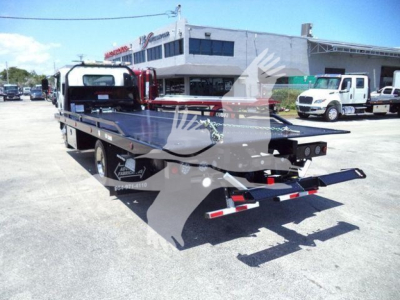Isuzu rollback tow truck with flatbed in lot; visible text on side includes 'LONE STAR', 'LOADED' logos and contact numbers; background shows dealership building and other trucks.