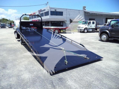 Isuzu NPR rollback truck with a flatbed in a dealership lot, showing the long angled bed and tie-down hooks.