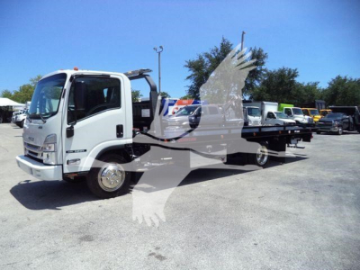 Isuzu NRR rollback truck in white with flatbed, side view showing cab and chassis, multiple trucks in lot in background.