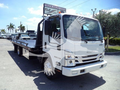 Isuzu NRR rollback truck in a lot showing a flatbed with dual rear wheels, cab with large windshield, and Isuzu emblem; signage and palm trees in background.