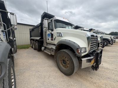 Mack GR84F dump truck in a used lot, front-left view showing chrome bumper and wheel, white cab with black dumping bed, other trucks in background.