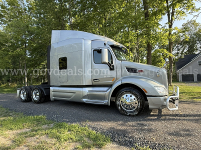 Peterbilt 579 semi-truck in silver, side view showing cab and dual rear axles, chrome wheels, black tires, daytime outdoor lot.