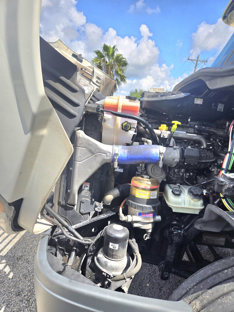 Truck engine bay of a 2019 Freightliner Cascadia midroof showing coolant reservoir, blue intercooler hose, air intake, and various reservoir caps.