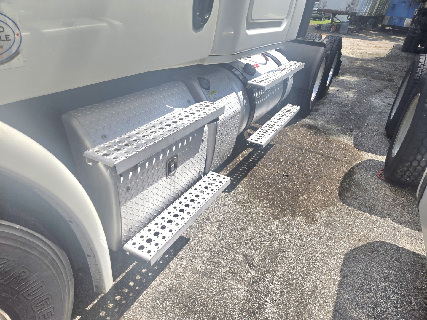 Truck side view showing aluminum diamond-plate fuel and storage steps on a Freightliner Cascadia midroof, twin rear axles, service area.