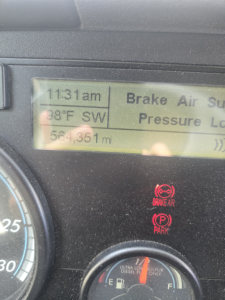 Dashboard display of a Freightliner Cascadia showing time 11:31am, 98°F SW, 564,351 mi and warning texts; brake air and park indicators.