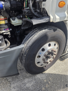 Freightliner Cascadia midroof front wheel well showing tire and wheel hub with engine bay components nearby
