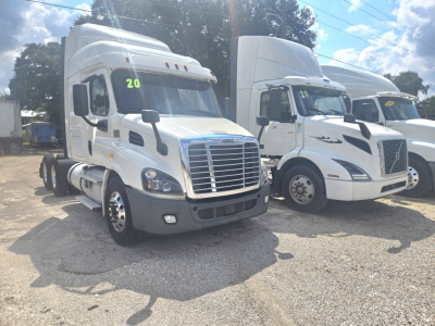 Truck cab showing Freightliner Cascadia midroof in a used-truck lot; white sleeper cab with side mirrors, grille, and front bumper visible; number 20 on windshield.
