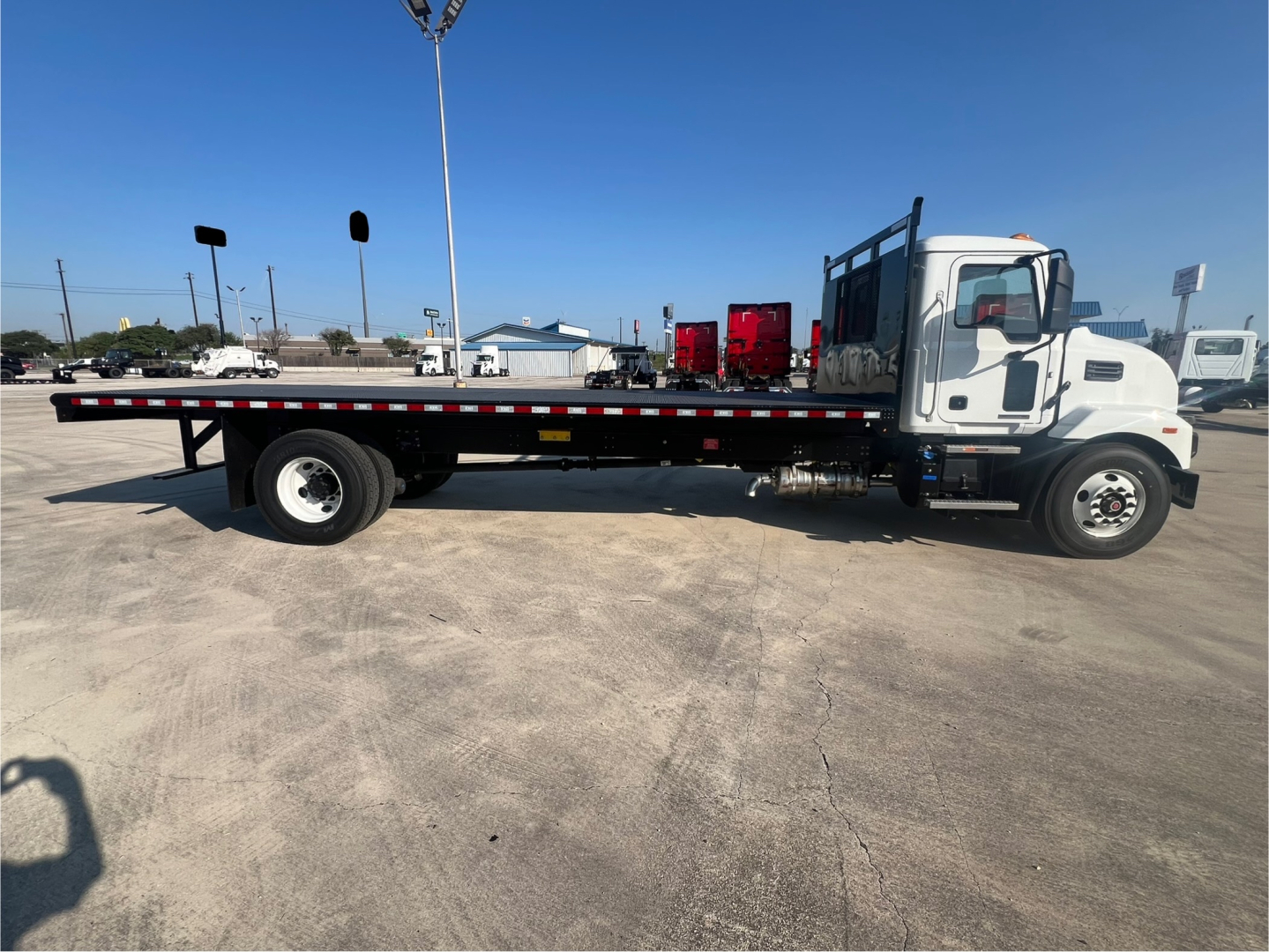 Flatbed truck side view showing Mack MD6 cab and long flatbed with dual rear wheels and spare tire mount. VIN 1M2MDBAAXTS019202 on listing, stock 69449.