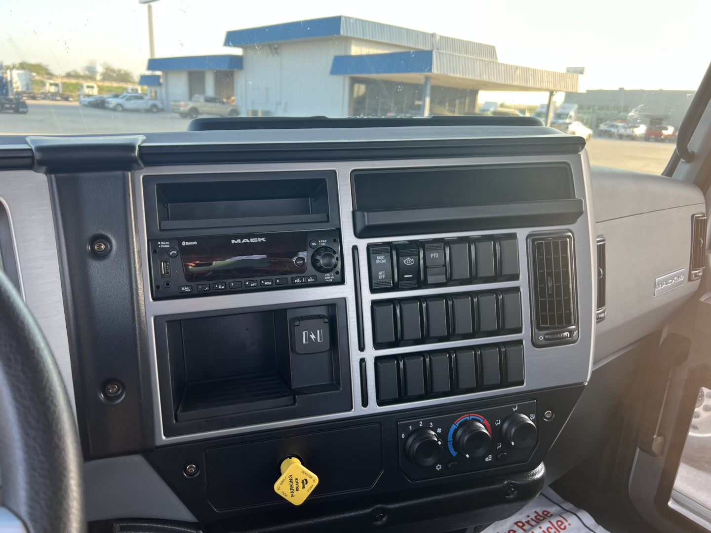 Dashboard of a 2026 Mack MD6 showing the infotainment head unit, climate controls, and multiple switches in a flatbed truck interior.