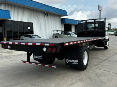 Flatbed truck chassis showing rear view of a 2026 Mack MD6 with a long flatbed, dual rear wheels, and Bruckner’s mud flaps.