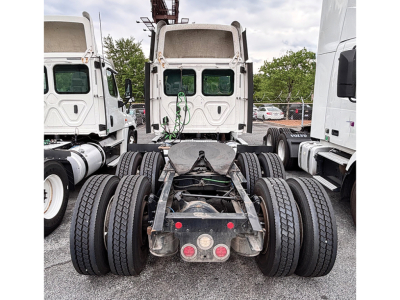 Freightliner truck chassis rear view showing dual rear axles and fifth wheel mounting under sleeper cab, with tires and green cables visible.