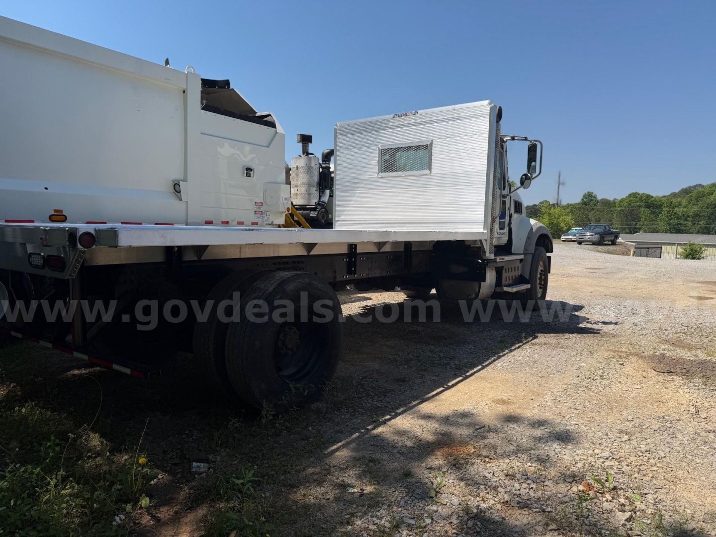 Flatbed truck on gravel lot with a white dump body and raised aluminum crew cab area, Mack Granite 2013 in background.