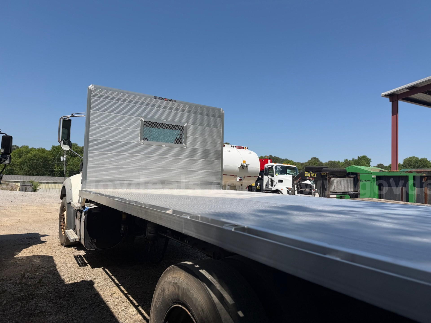 Flatbed tow truck bed with side panel and Mack Granite cab in background, utility equipment and open blue sky.