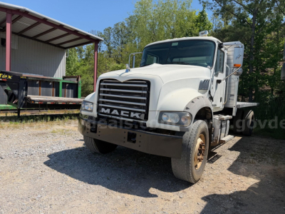 Mack Granite flatbed truck front view in daylight showing large grille, two headlights, and white cab with sleeper; stock number 18899-31 visible; off-road surface.