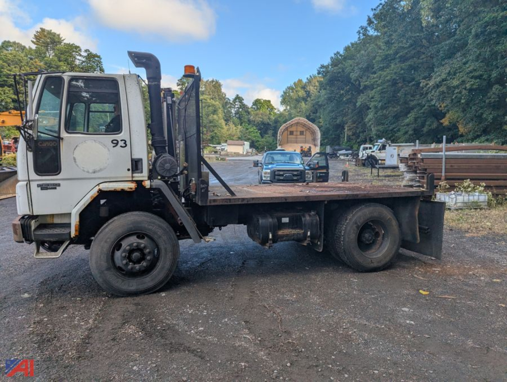 Flatbed truck chassis with a Freightliner FC80 cab, single rear axle, wood/metal deck, in-service condition.