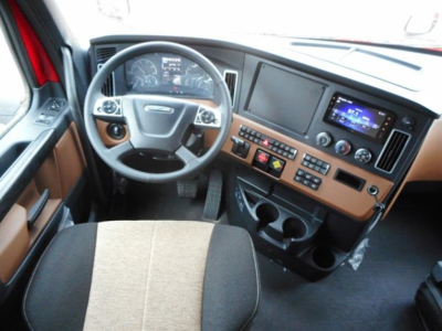 Cab interior of a new Freightliner Cascadia 126 showing steering wheel, dashboard with digital displays, center console with controls, and cup holders.