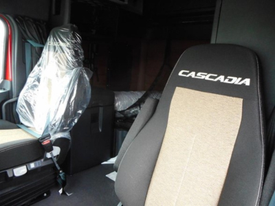 Truck cabin seat with 'CASCADIA' logo on headrest and plastic-covered seat in a new Freightliner Cascadia 126 truck interior.