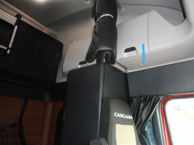 Interior view of a Freightliner Cascadia 126 sleeper cab showing seating area and overhead storage with CASCADIA branding on seat; partial driver window and door frame visible.