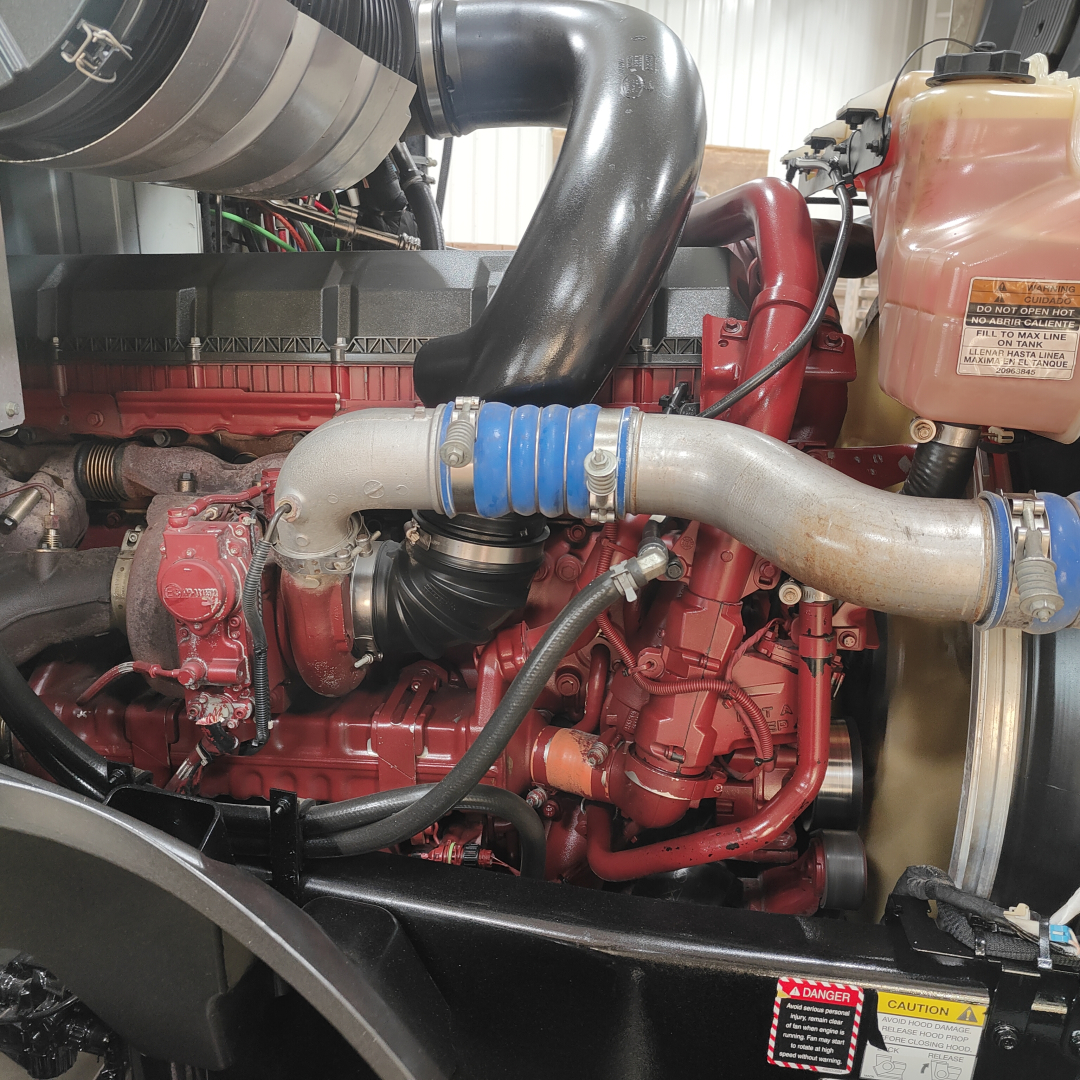 Mack AN64T engine bay showing turbocharger, intake piping, coolant reservoir, and engine block with red paint and hoses.