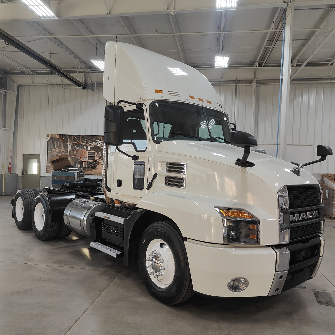 Mack AN64T tractor in a showroom setting, front three-quarter view, white cab with black accents, DEF and fuel tanks visible, no license plate.