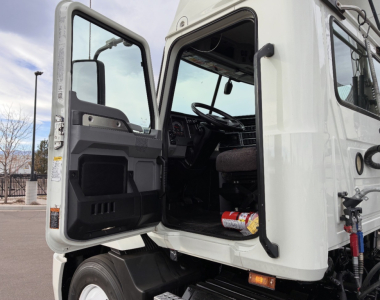 Truck cab interior open door of 2020 Mack AN64T showing steering wheel and driver's seat with dashboard, exterior cab white.