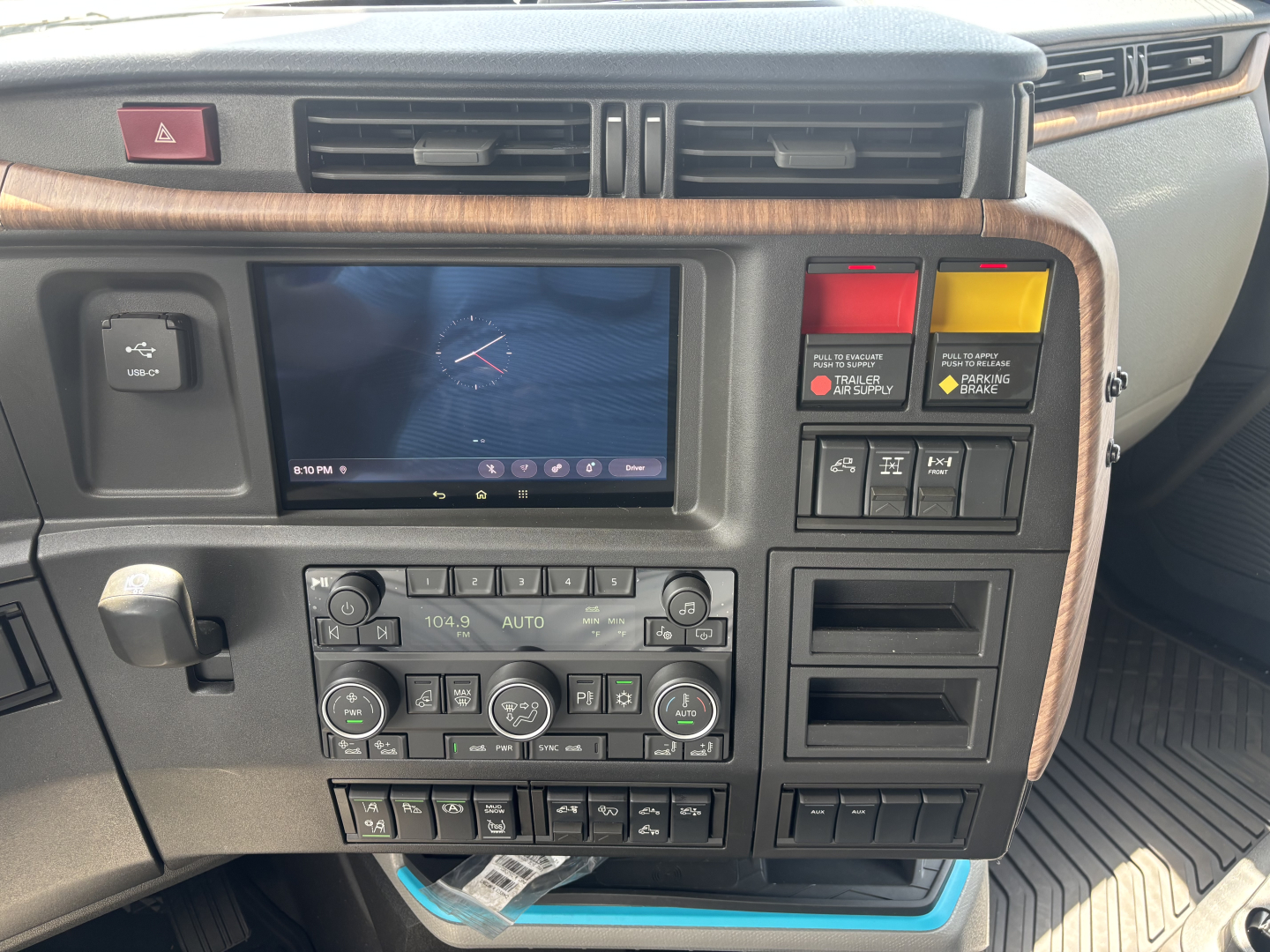 Dashboard of a Volvo truck interior showing infotainment screen, climate controls, and various labeled switches and warning lights.
